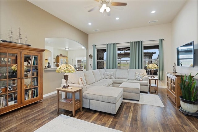 living room with dark wood-type flooring, arched walkways, visible vents, and lofted ceiling