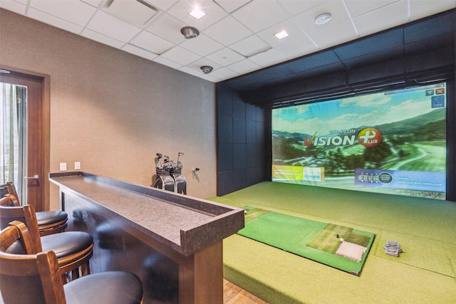 recreation room with golf simulator, a drop ceiling, and a dry bar