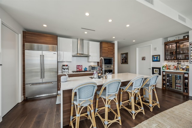 kitchen featuring dark wood finished floors, light countertops, modern cabinets, built in appliances, and wall chimney exhaust hood