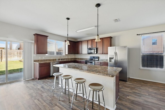 kitchen featuring a breakfast bar area, stainless steel appliances, a sink, a center island, and dark wood finished floors