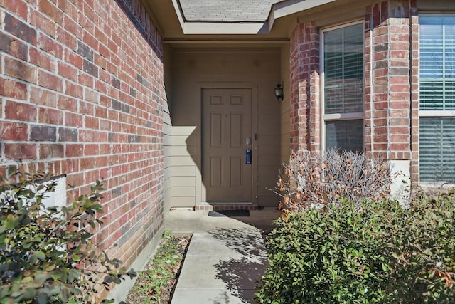 property entrance featuring brick siding and roof with shingles