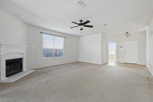 unfurnished living room featuring a ceiling fan, visible vents, a fireplace with raised hearth, and carpet flooring