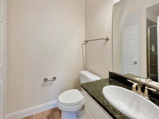 bathroom featuring toilet, wood finished floors, vanity, baseboards, and a shower with door