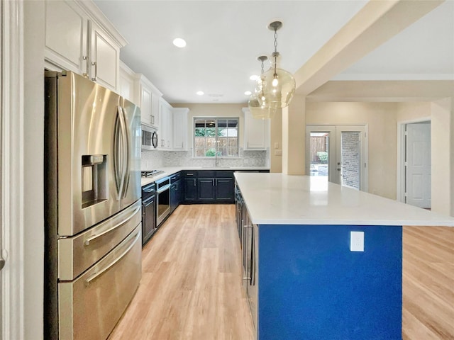 kitchen with stainless steel appliances, light countertops, light wood-type flooring, backsplash, and a center island