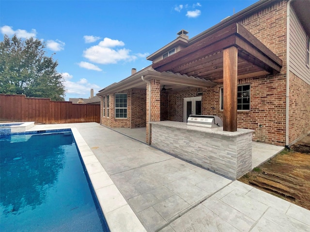 view of swimming pool featuring a patio, a pool with connected hot tub, grilling area, exterior kitchen, and a fenced backyard