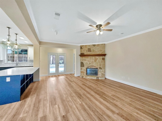 unfurnished living room featuring light wood-type flooring, ornamental molding, french doors, and a stone fireplace