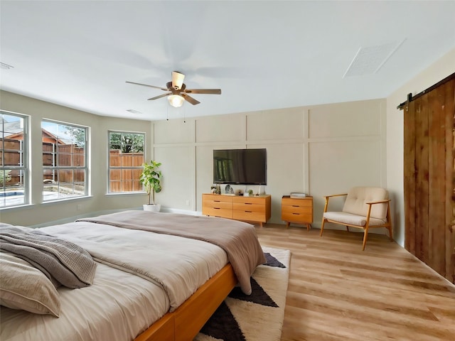 bedroom with a barn door, visible vents, a ceiling fan, light wood-type flooring, and a decorative wall