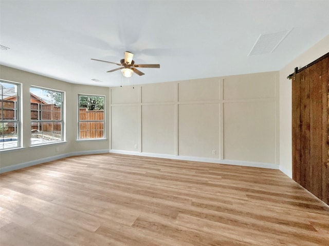 unfurnished room featuring light wood-style floors, a ceiling fan, a decorative wall, and a barn door