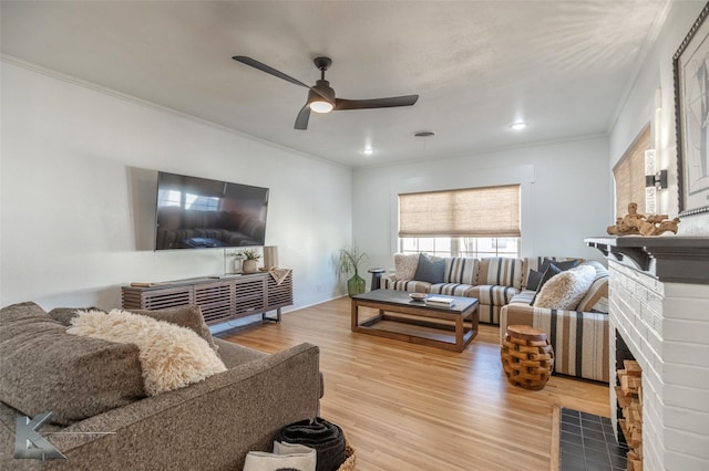 living area with baseboards, ceiling fan, ornamental molding, wood finished floors, and a brick fireplace