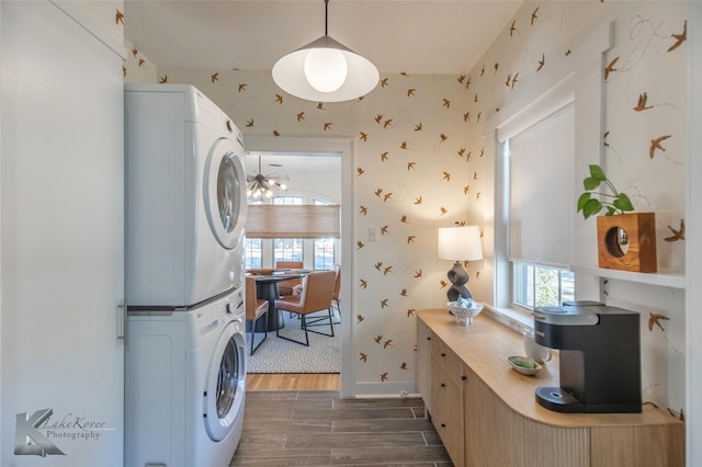 washroom featuring stacked washer and dryer, laundry area, a healthy amount of sunlight, wood tiled floor, and wallpapered walls