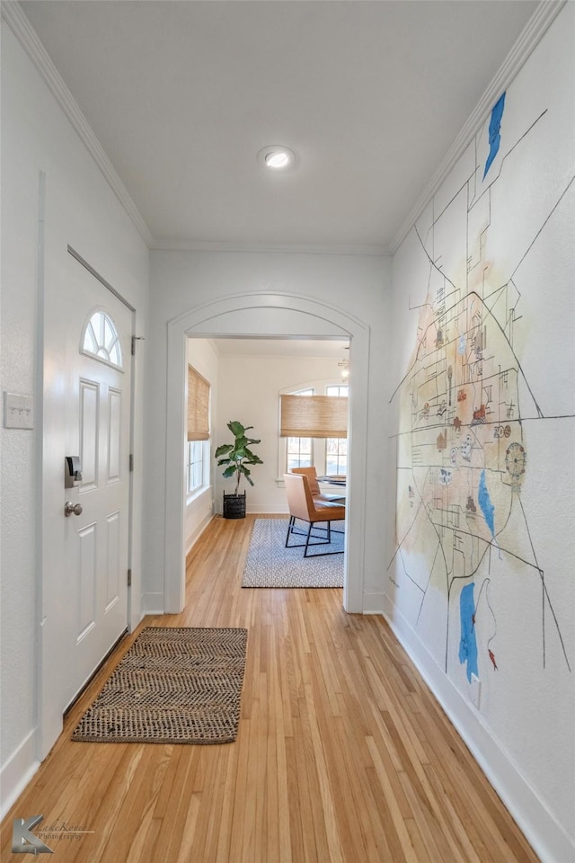 foyer featuring light wood-style floors, baseboards, ornamental molding, and arched walkways