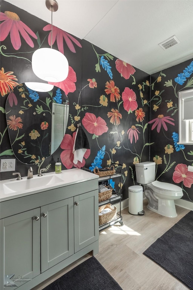 bathroom featuring visible vents, toilet, vanity, wood finished floors, and baseboards