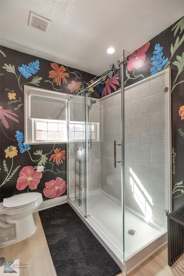 bathroom with a stall shower, visible vents, toilet, and wood finished floors