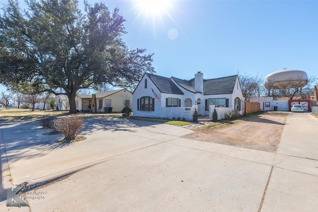 view of front of house with stucco siding, driveway, a chimney, and fence