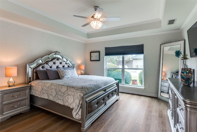 bedroom with dark wood-style floors, a tray ceiling, visible vents, and ornamental molding