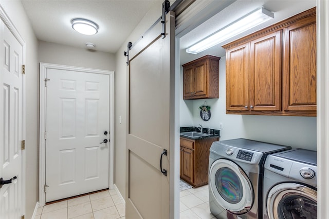 laundry room with cabinet space, a barn door, washing machine and dryer, light tile patterned flooring, and a sink