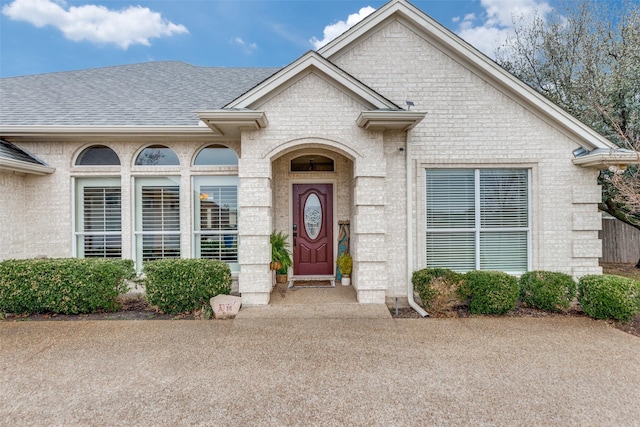 property entrance with a shingled roof and brick siding