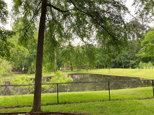 view of community featuring a yard, a water view, and fence