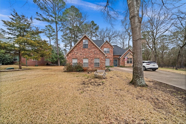 traditional home with brick siding, driveway, a front lawn, and roof with shingles