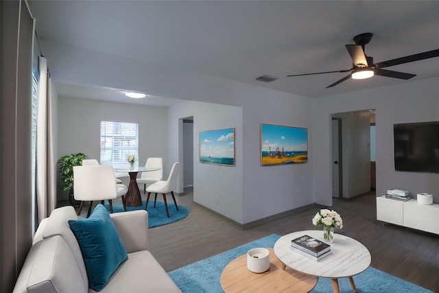 living room with ceiling fan, wood finished floors, visible vents, and baseboards