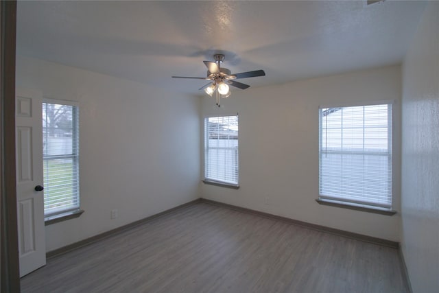 empty room with wood finished floors, a ceiling fan, and baseboards