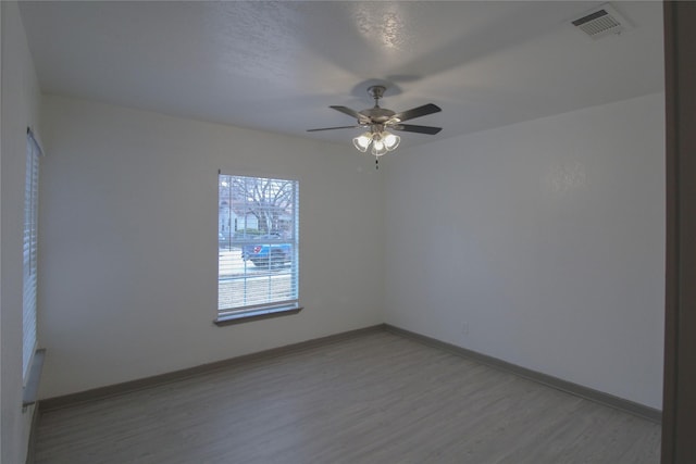 empty room with light wood finished floors, baseboards, visible vents, and a ceiling fan