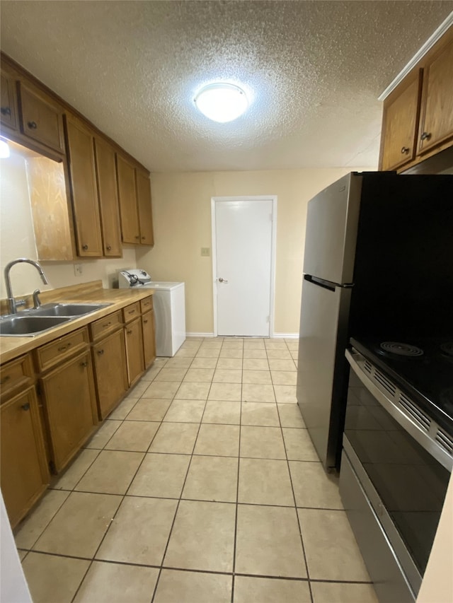 kitchen with light tile patterned floors, a sink, brown cabinets, stainless steel electric range oven, and washer / clothes dryer