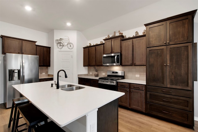 kitchen with a kitchen island with sink, light wood-style flooring, dark brown cabinetry, stainless steel appliances, and a sink