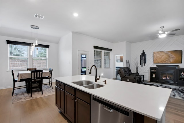 kitchen featuring open floor plan, a lit fireplace, stainless steel dishwasher, light wood-style floors, and a sink