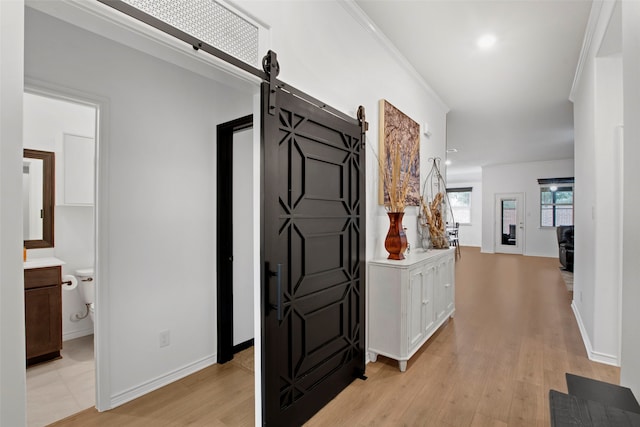 hall featuring light wood-type flooring, baseboards, and a barn door