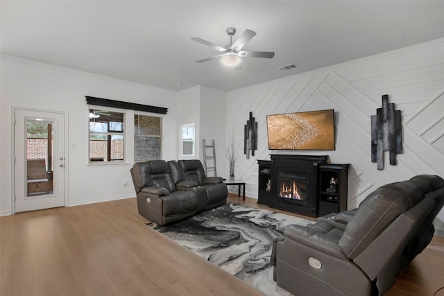 living area with baseboards, visible vents, a glass covered fireplace, ceiling fan, and wood finished floors