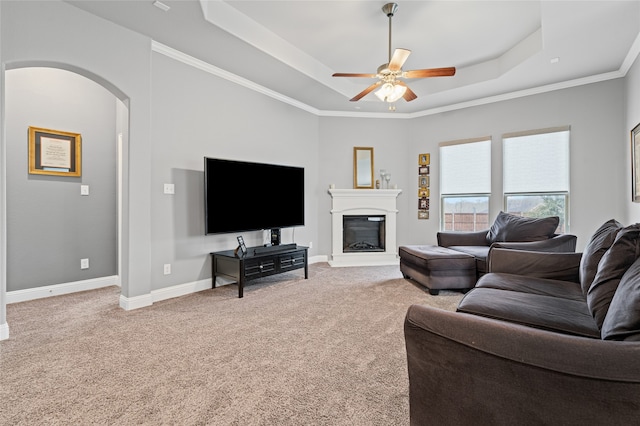 living room with baseboards, carpet, arched walkways, a glass covered fireplace, and a raised ceiling