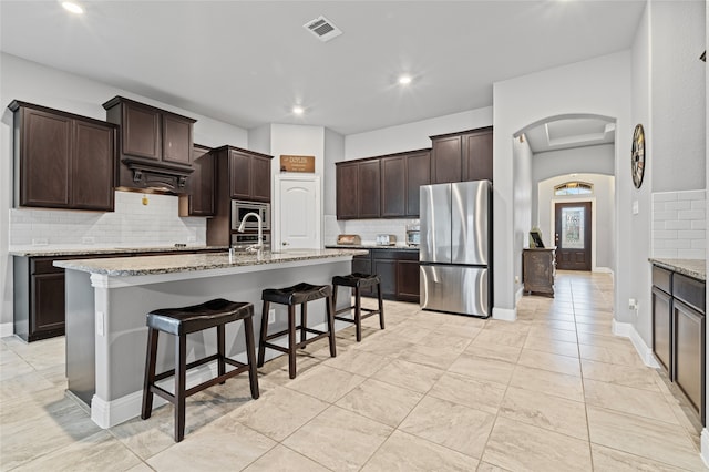 kitchen with visible vents, arched walkways, dark brown cabinetry, appliances with stainless steel finishes, and a breakfast bar area