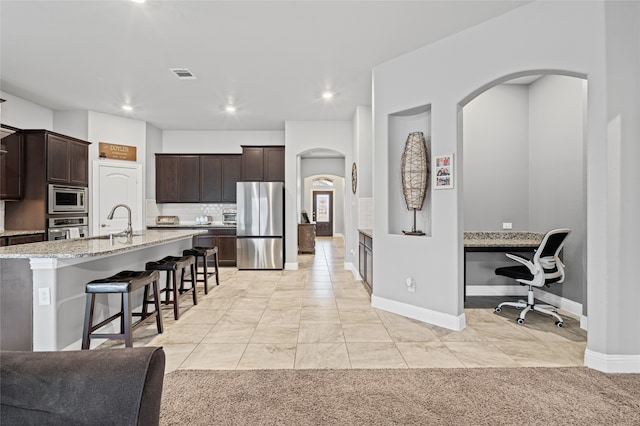 kitchen featuring visible vents, dark brown cabinetry, light stone counters, appliances with stainless steel finishes, and a kitchen breakfast bar