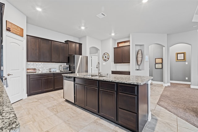 kitchen with visible vents, a sink, light stone counters, stainless steel appliances, and arched walkways