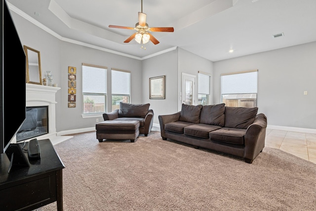 tiled living area with visible vents, a raised ceiling, baseboards, and a glass covered fireplace