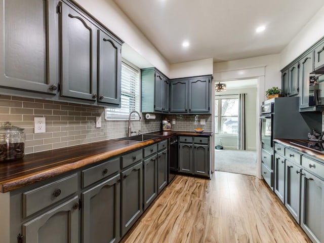 kitchen with wooden counters, light wood-style flooring, a sink, decorative backsplash, and black appliances