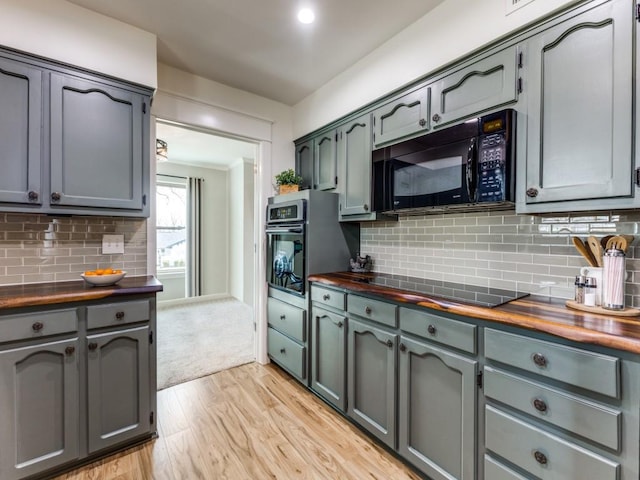 kitchen featuring tasteful backsplash, light wood-style flooring, wooden counters, and black appliances