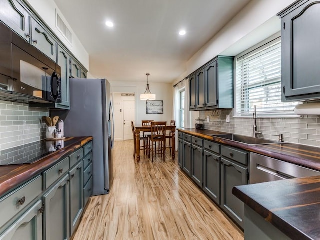 kitchen with light wood finished floors, backsplash, butcher block countertops, black appliances, and a sink