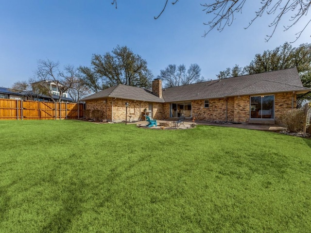 rear view of property featuring brick siding, fence, a lawn, a chimney, and a patio area