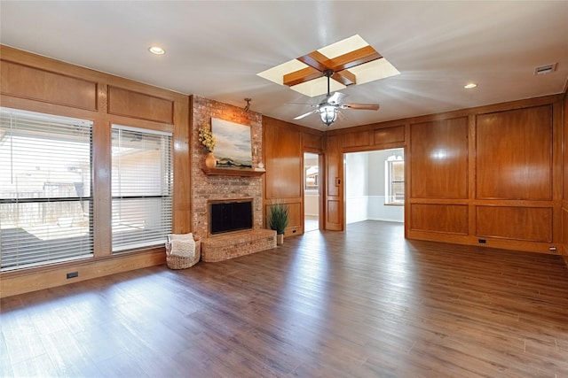 unfurnished living room featuring a fireplace, visible vents, a decorative wall, a ceiling fan, and wood finished floors