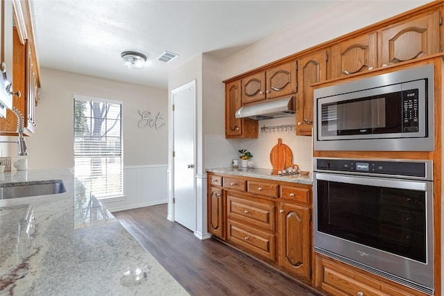 kitchen featuring under cabinet range hood, a wainscoted wall, visible vents, appliances with stainless steel finishes, and dark wood finished floors