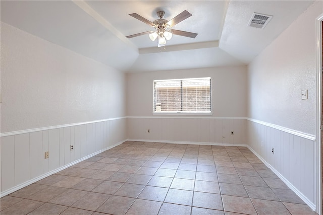 spare room featuring light tile patterned floors, visible vents, a ceiling fan, a wainscoted wall, and vaulted ceiling