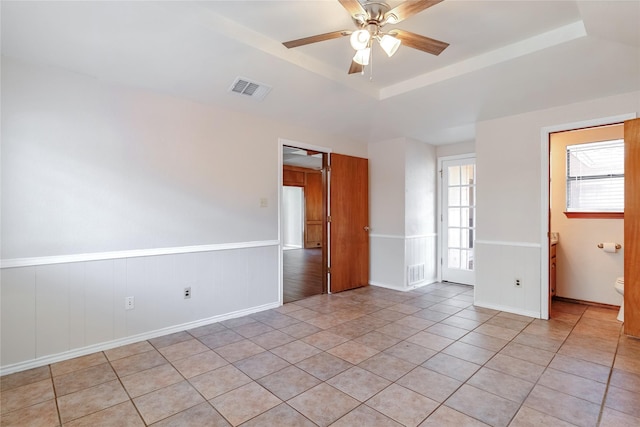 empty room featuring a wainscoted wall, a raised ceiling, visible vents, and a ceiling fan