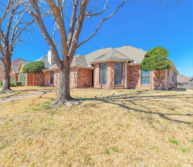 ranch-style house featuring roof with shingles, a front yard, and brick siding