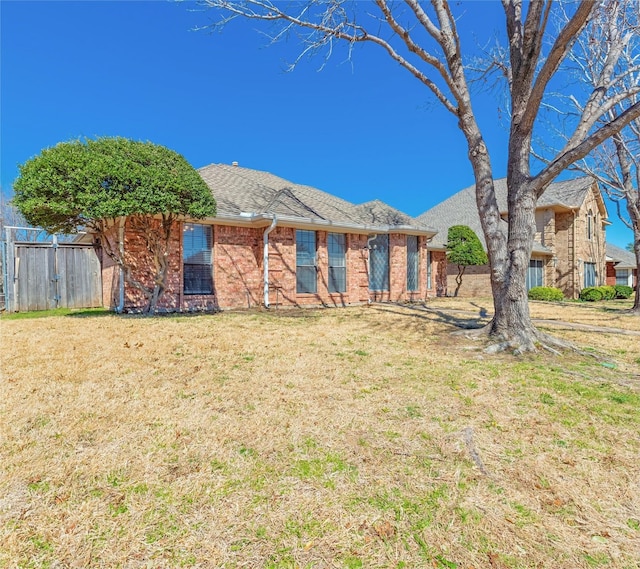 ranch-style home featuring a front lawn, a shingled roof, fence, and brick siding