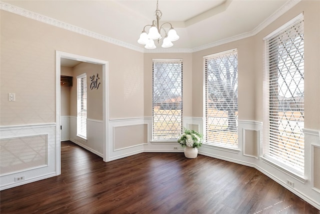 unfurnished dining area with dark wood-style floors, a tray ceiling, wainscoting, and a notable chandelier