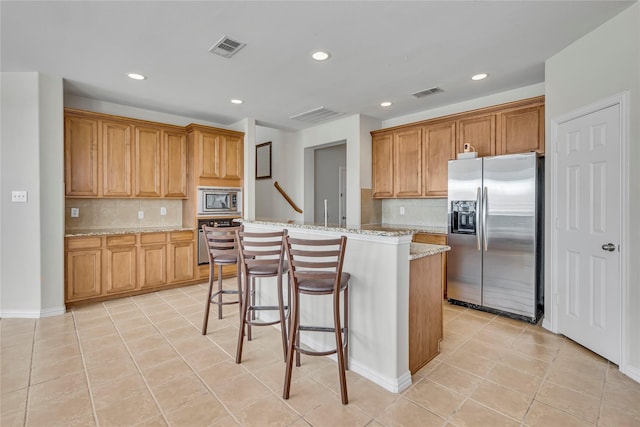 kitchen featuring light stone countertops, visible vents, a kitchen island, and appliances with stainless steel finishes