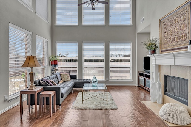 living room featuring baseboards, visible vents, a tiled fireplace, and wood finished floors