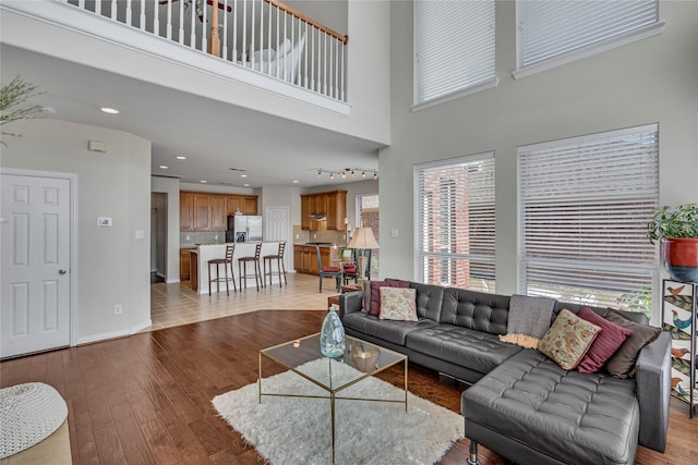 living room featuring baseboards, light wood finished floors, a towering ceiling, and recessed lighting